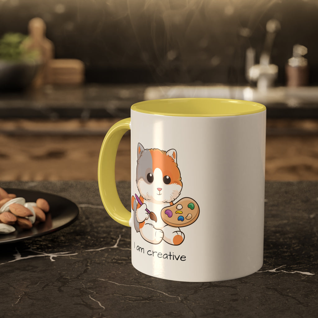 A white mug with a yellow handle and interior and a picture of a cat that says I am creative. The mug sits on a black kitchen counter and has steam rising out of it.