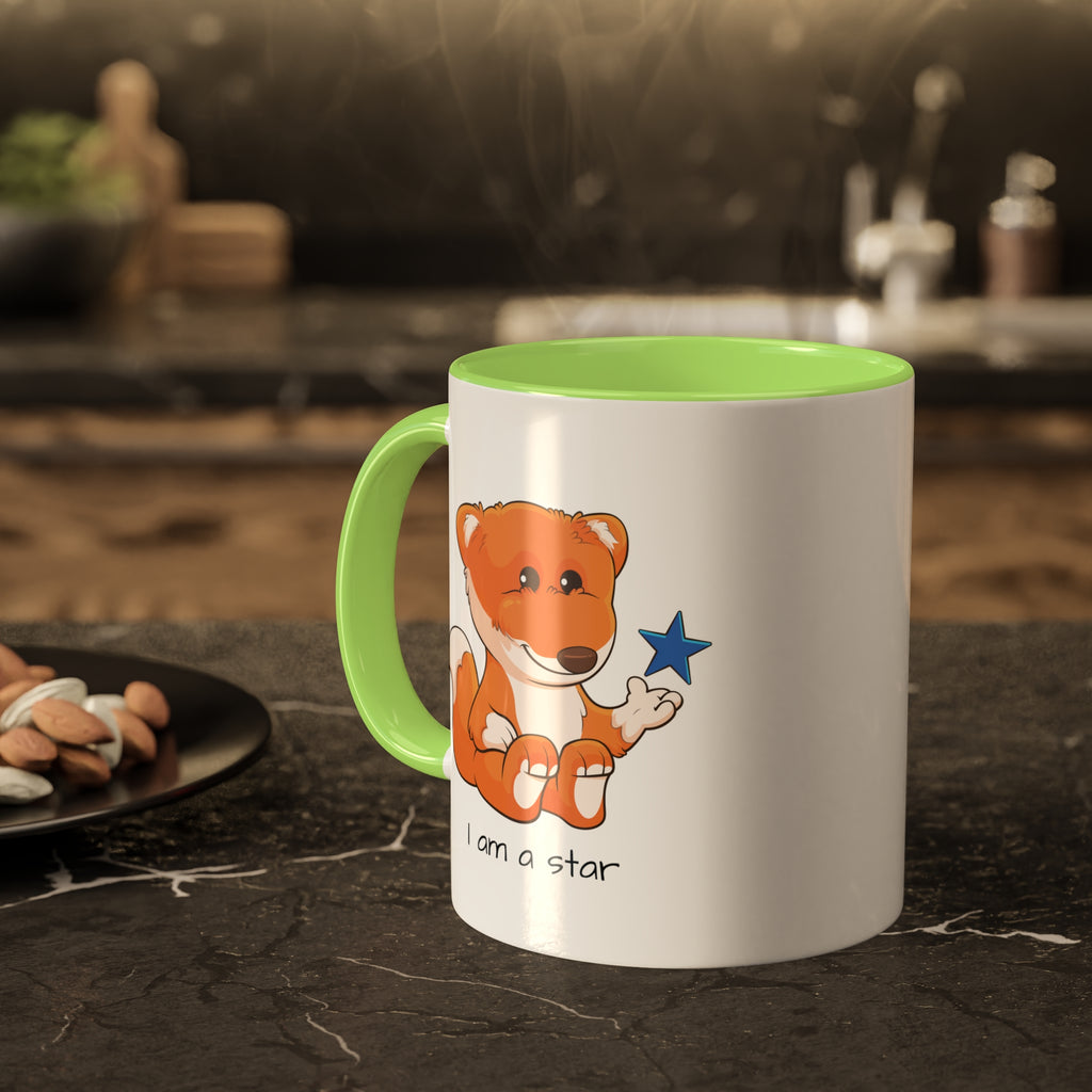 A white mug with a light green handle and interior and a picture of a fox that says I am a star. The mug sits on a black kitchen counter and has steam rising out of it.